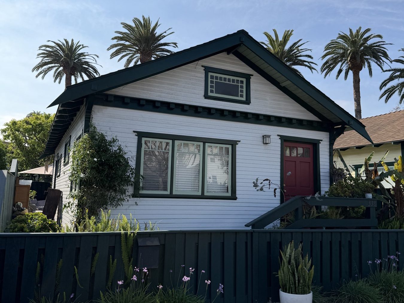 The 1920s Venice Beach bungalow gallery — white clapboard, dark green trim, red door, palms overhead